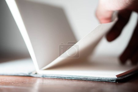 Close-up of a person flipping through the pages of a notebook on a wooden table.