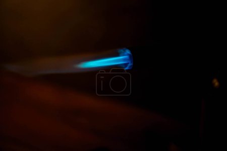 A close-up of a blue flame from a blowtorch against a dark background.