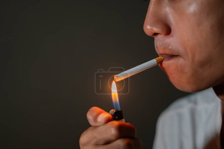 Close-up of a person lighting a cigarette with a lighter. The background is dark, and the focus is on the cigarette and the flame.