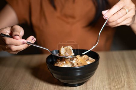 A person holding a bowl of beef and onion rice dish on a wooden table.