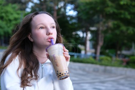 Photo for Delicious drink Bubble Tea drinking delicious coffee tea smoothie on the street a young girl happily pulls liquid from a straw chews swallows yami yami. High quality - Royalty Free Image