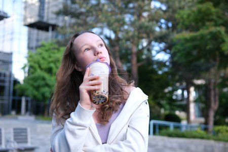 Photo for Delicious drink Bubble Tea drinking delicious coffee tea smoothie on the street a young girl happily pulls liquid from a straw chews swallows yami yami. High quality - Royalty Free Image