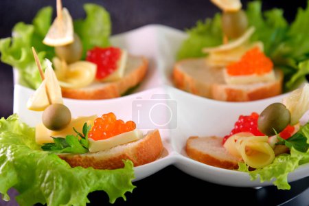Photo for Four sandwiches with red caviar on a white plate, French croissant, lemon slice, olive, piece of cheese, fresh green lettuce. High quality photo - Royalty Free Image