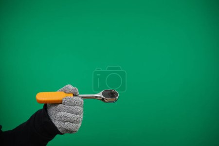 Photo for Ratchet wrench, short ratchet, mini ratchet wrench, quick release chrome molybdenum steel reversible socket, chrome plated steel. close-up, hand with gray gloves. Green background chromakey - Royalty Free Image