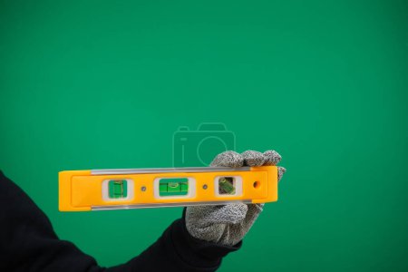Building level. Hand in gloves holds a yellow building level advertising Green background chromakey free space. Postcard or poster for print, place for text. High quality