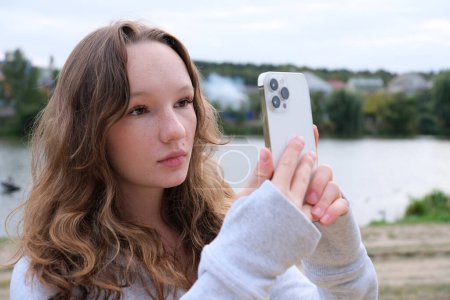 Red-haired young girl taking selfie with her smartphone against snowy background. Selective focus. High quality photo