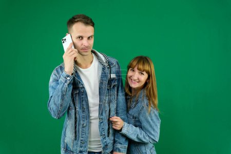 Cheerful guy and girl in denim clothes, couple, family. guy calling on the phone on a green background. High quality photo