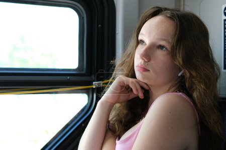 The girl puts on headphones, listens to audio messages and music, listens to songs and podcasts on an online application. Language learning on public transport. Keeping a teenager quiet in a public