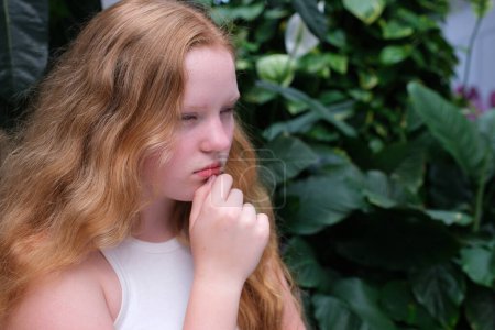 The girl, red-haired, put her hand to her chin, thinking, thinking, dreaming. High quality photo
