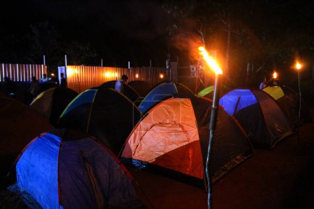 Photo for You can see a camp with conical tents lined up surrounded by torches at night - Royalty Free Image