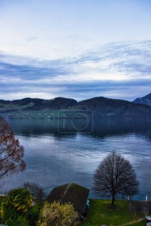 Téléchargez les photos : Panorama bleu sur le lac au crépuscule : vue paisible avec arbres, eau, montagnes et ciel. - en image libre de droit