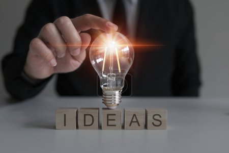 Photo for Hand touching a light bulb on a wooden block with the words Ideas, innovative and inspirational new concept, innovative technology. - Royalty Free Image