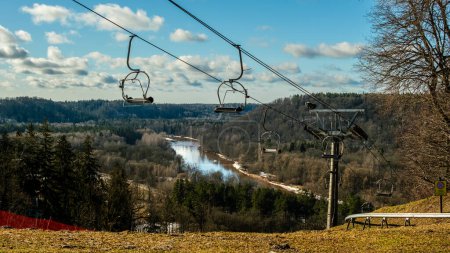 Against the backdrop of a sunlit winter day, Sigulda's chairlift offers a scenic journey over the tranquil waters of River Gauja, showcasing the beauty of Latvia's winter landscape.