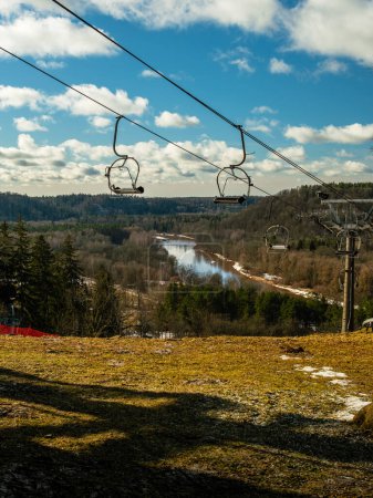A sunny winter day casts a golden glow as Sigulda's chairlift glides above the snow-covered banks of River Gauja, providing breathtaking views of this picturesque Latvian setting.