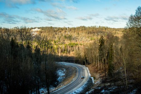 A sun-kissed winter day illuminates the winding road through Sigulda, Latvia, offering a picturesque journey amidst snow-cloaked landscapes.