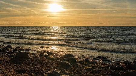 Veczemju Klintis, Latvija, unveils its golden charm as the sun dips below the horizon, casting a radiant glow over the rocky beach during sunset's golden hour.