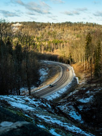 Foto de En Sigulda, Letonia, las suaves curvas del camino se entrelazan a través de un país de las maravillas invernales, donde la luz del sol baila sobre árboles cubiertos de nieve, creando una escena fascinante de belleza natural.. - Imagen libre de derechos