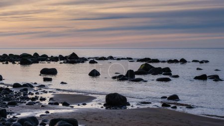 As day transitions into night, Veczemju Klintis offers a glimpse of coastal magic, with the rocky beach coast bathed in the ethereal light of twilight during sunset