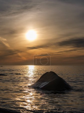 En la tranquila soledad de los mares de Veczemju Klintis, una piedra solitaria se deleita en el cálido resplandor de la puesta del sol, invitando a momentos de introspección y calma.