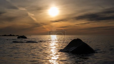 In der Umarmung der Dämmerung ruht ein einsamer Stein friedlich im Meer von Veczemju Klintis, ein stiller Beobachter der abendlichen Träumerei, die über den Horizont gemalt wird.