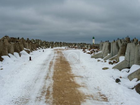 Un chemin gelé mène à Ventspils Southern Pier and Lighthouse, un voyage tranquille au milieu de l'étreinte de l'hiver.