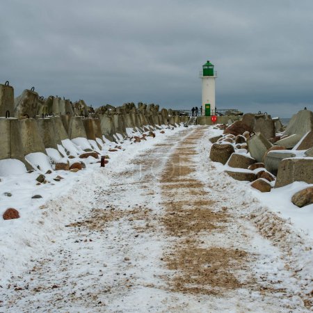 Traversant le paysage hivernal, le sentier se déploie vers Ventspils Southern Pier and Lighthouse, une scène pittoresque d'une beauté glacée.
