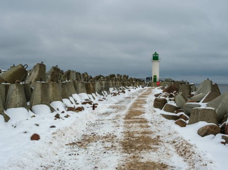 Sous une couverture de neige, le sentier fait signe à Ventspils Southern Pier and Lighthouse, offrant un aperçu serein de l'histoire maritime au milieu du froid hivernal..