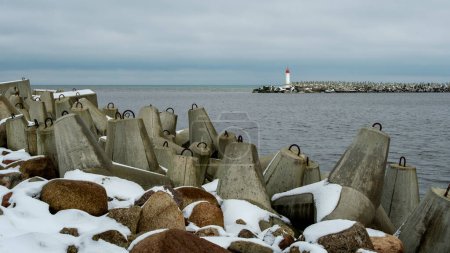 Ein ruhiges Küstenpanorama entfaltet sich am Nordpier von Ventspils, wo die Ostsee in ruhiger Umarmung auf die schneebedeckten Küsten trifft und zur Besinnung inmitten der Pracht der Natur einlädt..