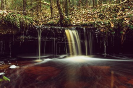 En el silencio de la larga exposición, las aguas en cascada de la cascada de Olupite se desdibujan en un tapiz de ensueño, que encarna el encanto sereno de Letonia.
