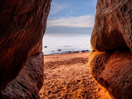 Alors que la lumière du jour décline, la grotte de Veczemju Klintis devient un havre de paix pour les amateurs de coucher de soleil, offrant un siège au premier rang de la symphonie nocturne de couleurs de la nature sur la plage rocheuse.