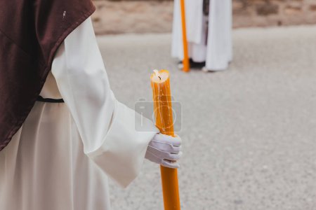 Holy Week procession with nazarenes carrying a large candle, holy week concept.