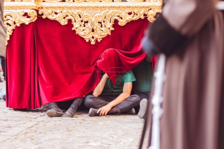 Téléchargez les photos : Personne avec le visage couvert assis sur le sol sous un trône de la semaine sainte se reposant pendant la journée. - en image libre de droit