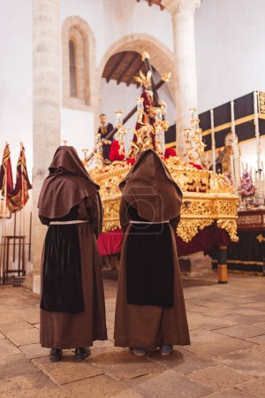 Téléchargez les photos : Couple de pénitents avec le dos tourné à contempler un trône de la Semaine Sainte. - en image libre de droit