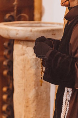 Téléchargez les photos : Gros plan des mains d'un pénitent priant le chapelet avec de l'eau bénite en arrière-plan - en image libre de droit
