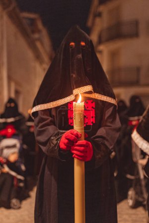 Téléchargez les photos : Pénitent devant avec capuche noire et gants rouges avec une bougie allumée dans ses mains en procession - en image libre de droit