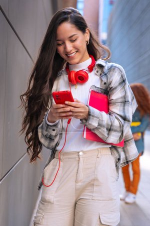 Téléchargez les photos : Jeune étudiant souriant avec ordinateur portable à la main utilise les réseaux sociaux avec des applications smartphone et la technologie sans fil à l'extérieur. - en image libre de droit