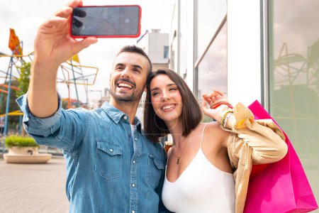 Téléchargez les photos : Happy shopping amis prendre une photo d'eux-mêmes sur smartphone s'amuser debout dans l'hypermarché. Les conjoints profitent du week-end dans un centre commercial moderne. Vendredi noir - en image libre de droit