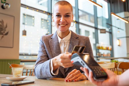 Foto de Mujer feliz sosteniendo una tarjeta de crédito y haciendo una transacción de pago mirando a la cámara - Imagen libre de derechos