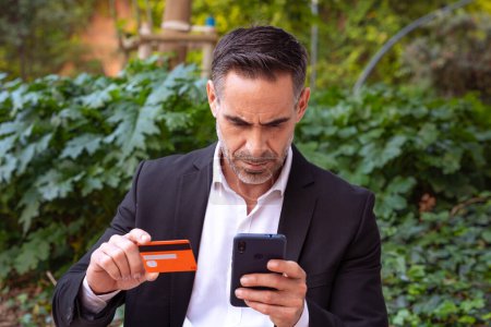 Téléchargez les photos : Homme avec carte de crédit et téléphone portable dans ses mains à l'extérieur. Concept : Achats en ligne. - en image libre de droit