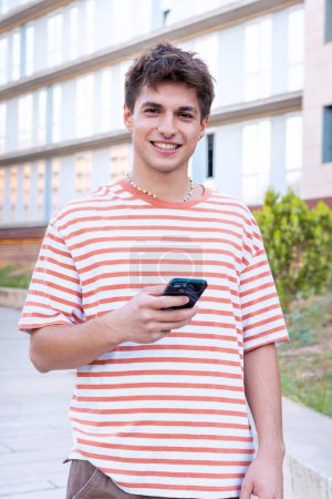 Foto de El estudiante feliz está dentro del campus universitario usando una aplicación de redes sociales. Vida universitaria - Imagen libre de derechos