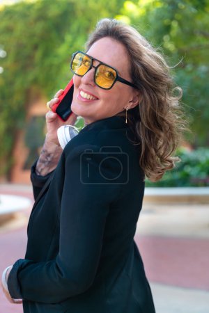 Photo for Side view portrait beautiful business woman wearing glasses,smiling talking on smart phone looking at camera. - Royalty Free Image