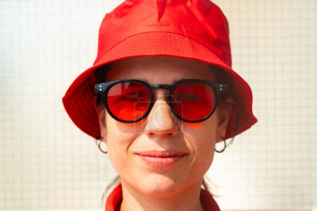 Téléchargez les photos : Élégante jeune femme souriante et regardant la caméra avec des lunettes et chapeau rouge.rait d'une belle femme caucasienne portant chapeau rouge et lunettes souriantes regardant la caméra. - en image libre de droit