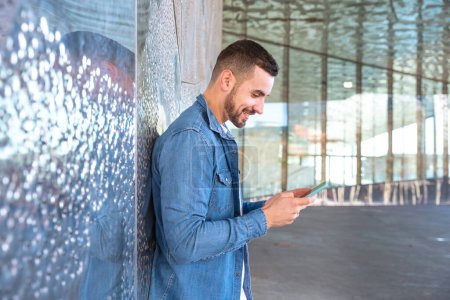 Téléchargez les photos : Jeune homme riant en utilisant les réseaux sociaux avec une application sur son téléphone portable. - en image libre de droit