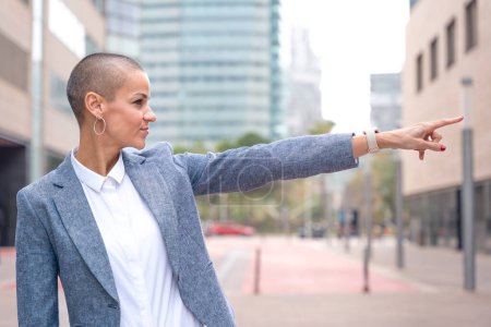 Photo for Confident middle-aged adult pointing finger at the left side of the logo. Woman showing signs Smiling young woman pointing finger to the side outdoors. - Royalty Free Image