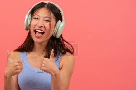 Photo for Beautiful young Asian woman wearing headphones pointing hands fingers up on the left side of the photo with a happy face. The girl standing in the studio. Advertising Presentation Concept - Royalty Free Image