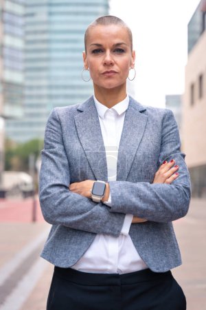 Photo for Close-up of a caucasian businesswoman looking seriously at the camera in a suit standing in outdoor workspace. Front view of a young lawyer with thoughtful expression staring. - Royalty Free Image