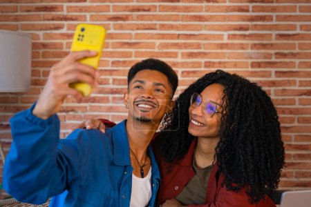 Foto de Una pareja multiétnica usando un teléfono inteligente se hace sonreír en casa, un novio latino y una novia afroamericana en las redes sociales prueban una nueva aplicación móvil - Imagen libre de derechos