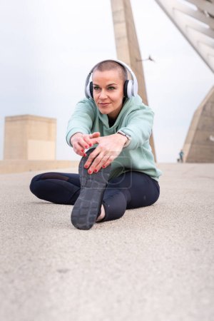 Photo for Sporty woman with sports headphones doing stretching sitting concentrated outdoors. - Royalty Free Image