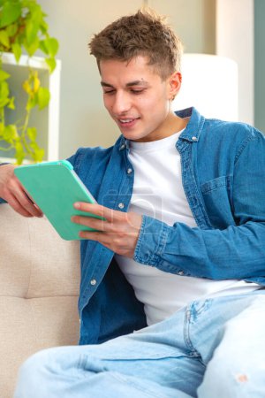 Téléchargez les photos : Jeune adulte sur canapé heureux achats en ligne avec tablette pc pour faire des paiements électroniques à distance facile et sécurisé.Intérieur - en image libre de droit