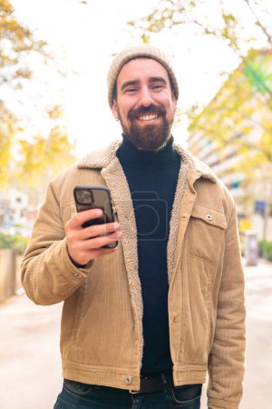  Portrait of a happy man looking at camera, smiling, sending messages using an app celular phone. Concept of human emotions, facial expression. 